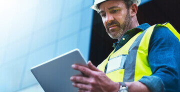 Worker in hard hat and vest looking at tablet